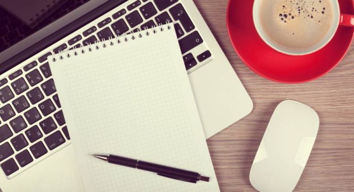 Blank notepad over laptop and coffee cup on office wooden table